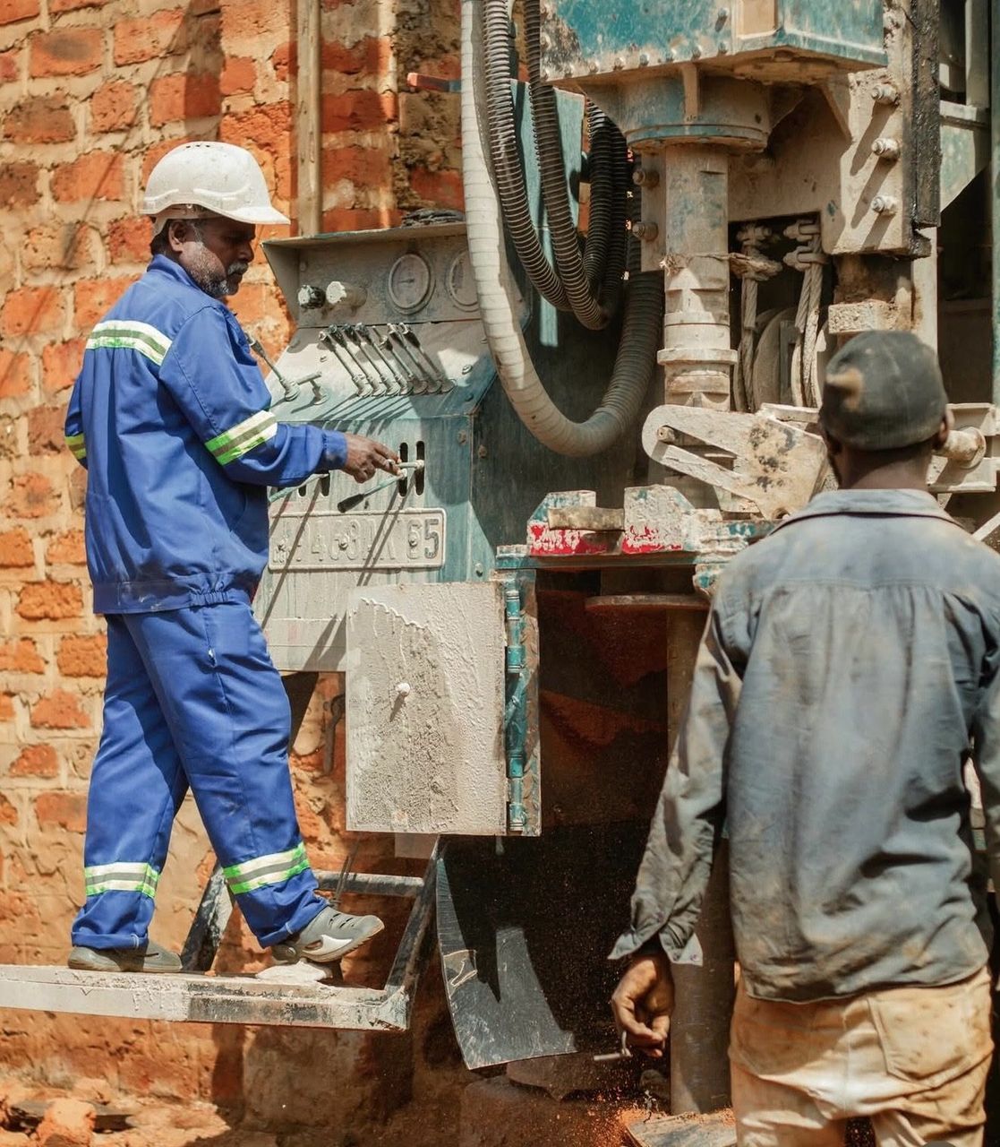 A technician in blue coveralls and a helmet operates the drilling rig controls in Lubumbashi