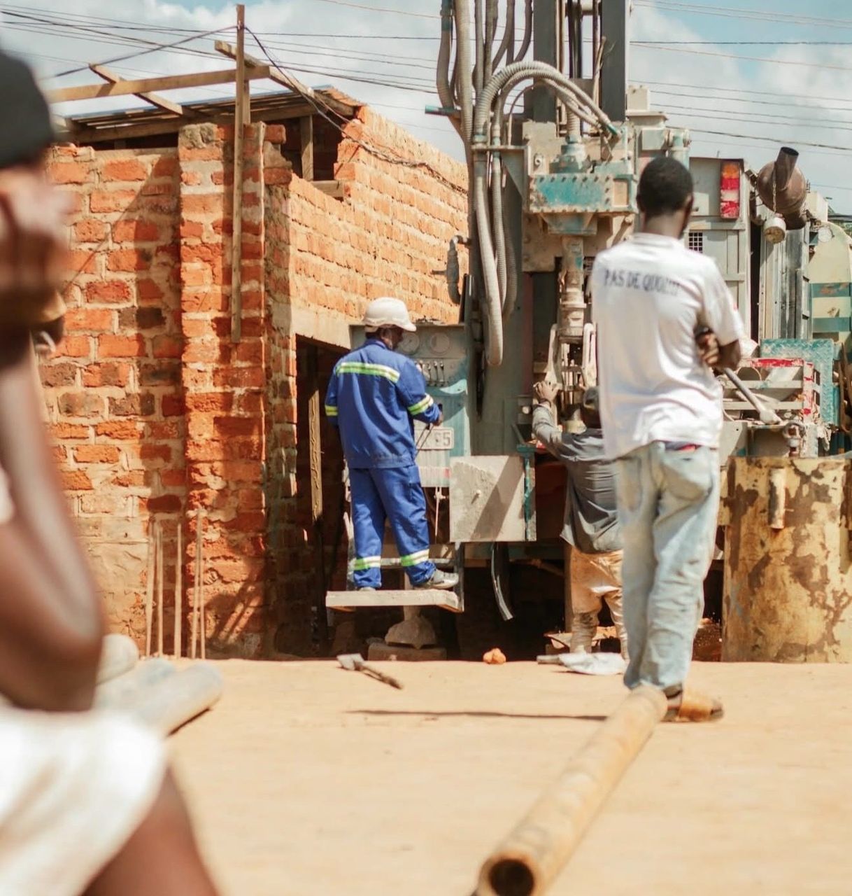 The drilling crew works together at the borehole site beside a brick wall in Lubumbashi